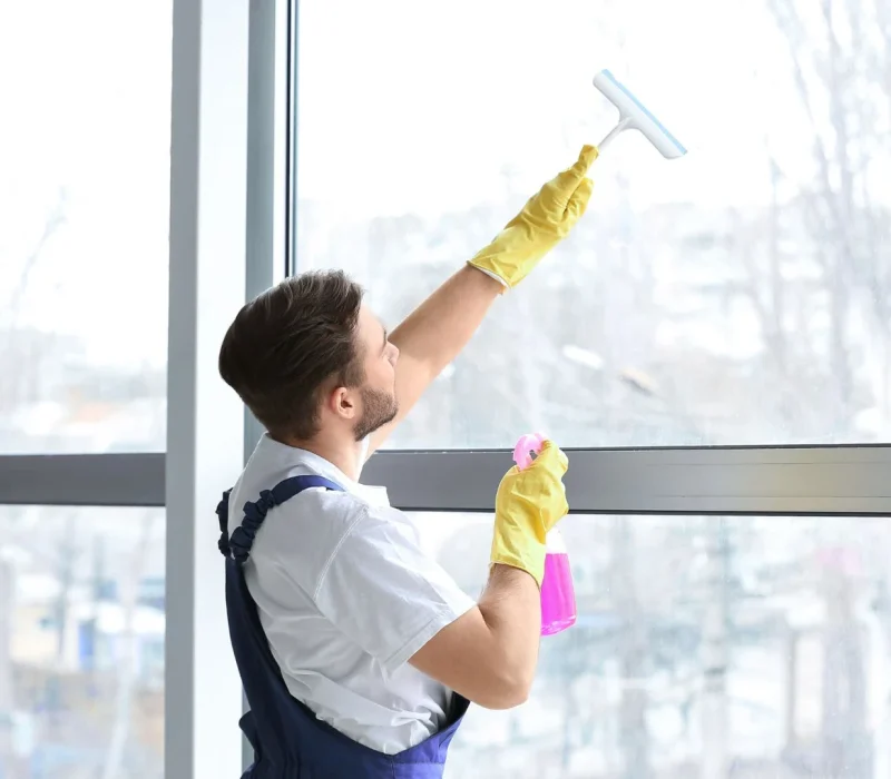 Male Janitor Cleaning Window in Office